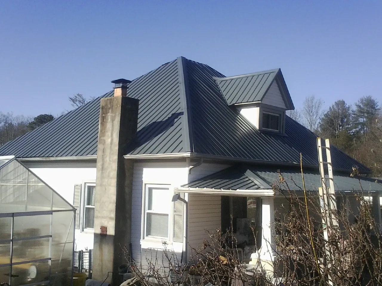 Dark blue standing seam metal roof on a white farmhouse with dormer — Slate & Tile Roof Repair by Roofing Brothers in Granite Falls