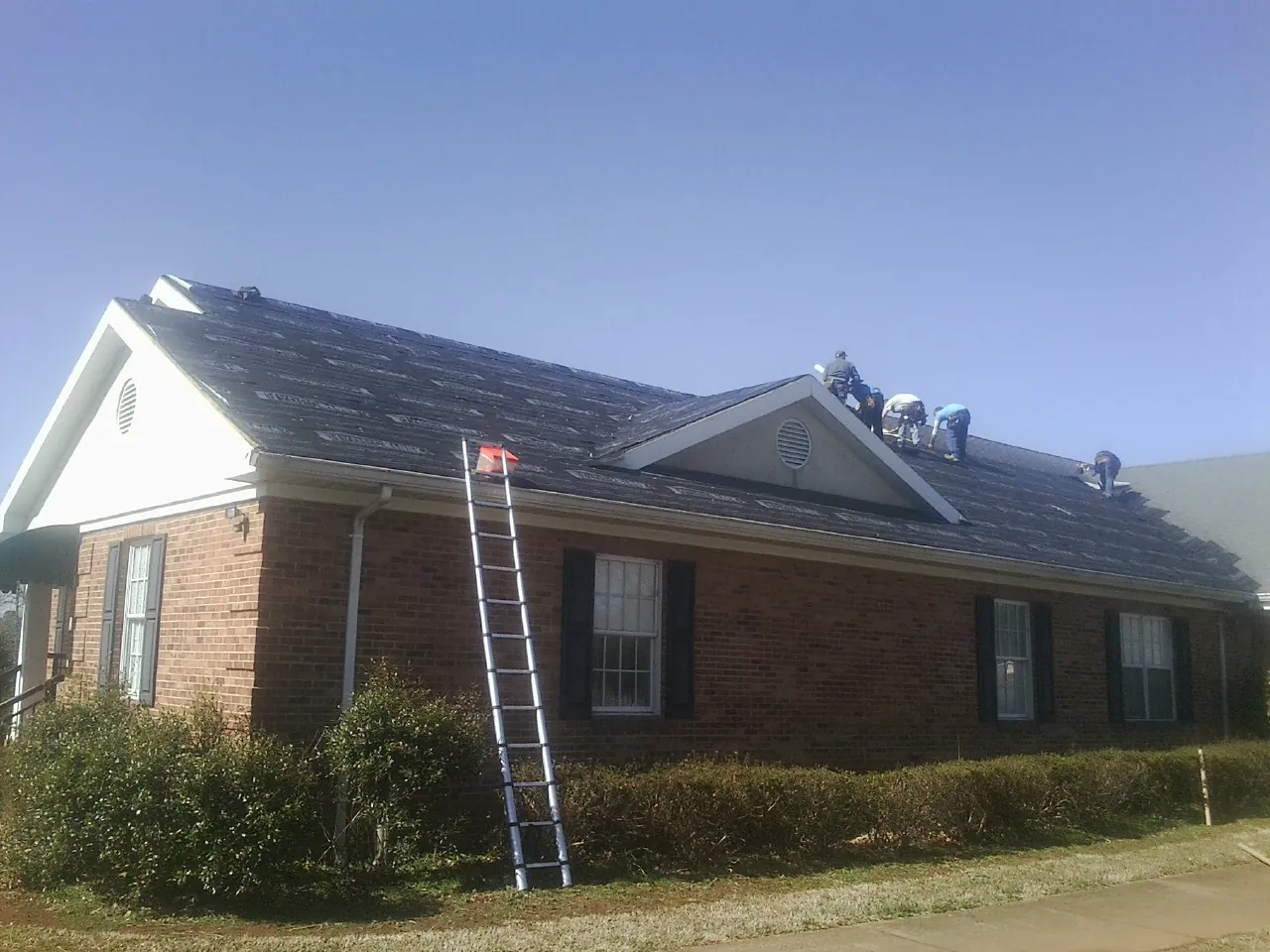 Crew tearing shingles off a brick ranch roof with a ladder set — Metal Roof Repair work by our crew in Granite Falls