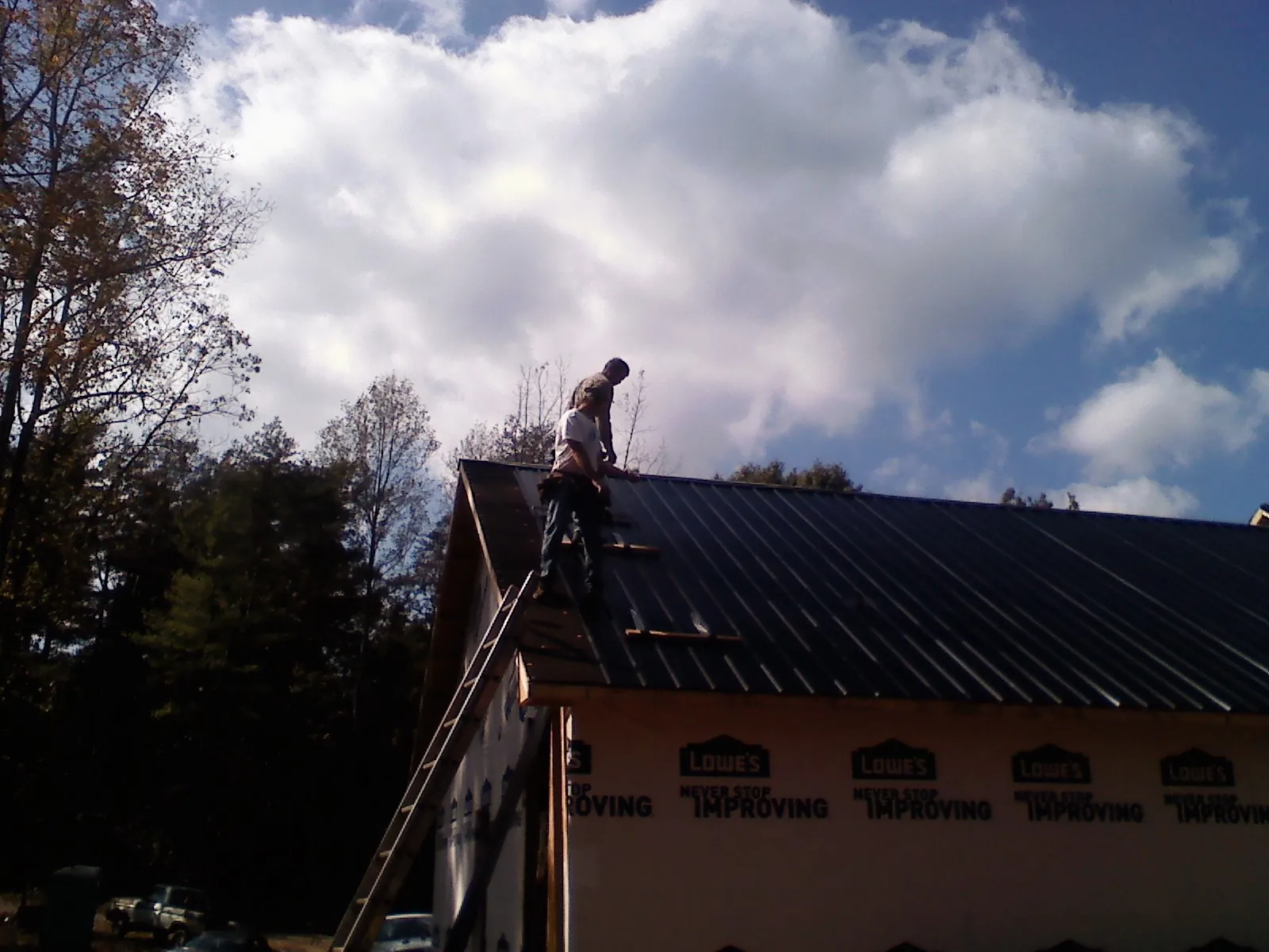 Roofer fastening dark metal panels high against a cloudy sky, from a Roof Inspection job in Granite Falls