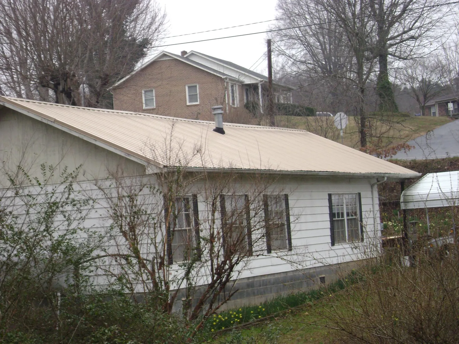 Tan metal roof on a white sided house set into a hillside in Granite Falls